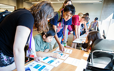 Three Scholars and Interns are gathered around a table and pointing at the optical illusions on the table.