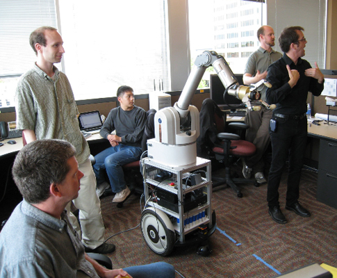 Picture of students and staff around a robotic arm.